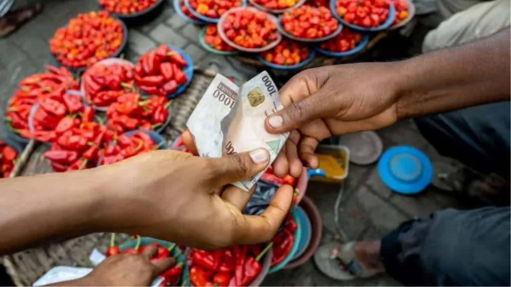 A photo of two hands holding a naira bill at an open market place
